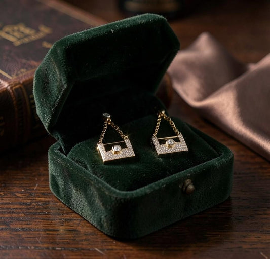Anzora Jewel Celaeno gold earrings with pavé diamonds in a dark green velvet jewelry box on a wooden table
