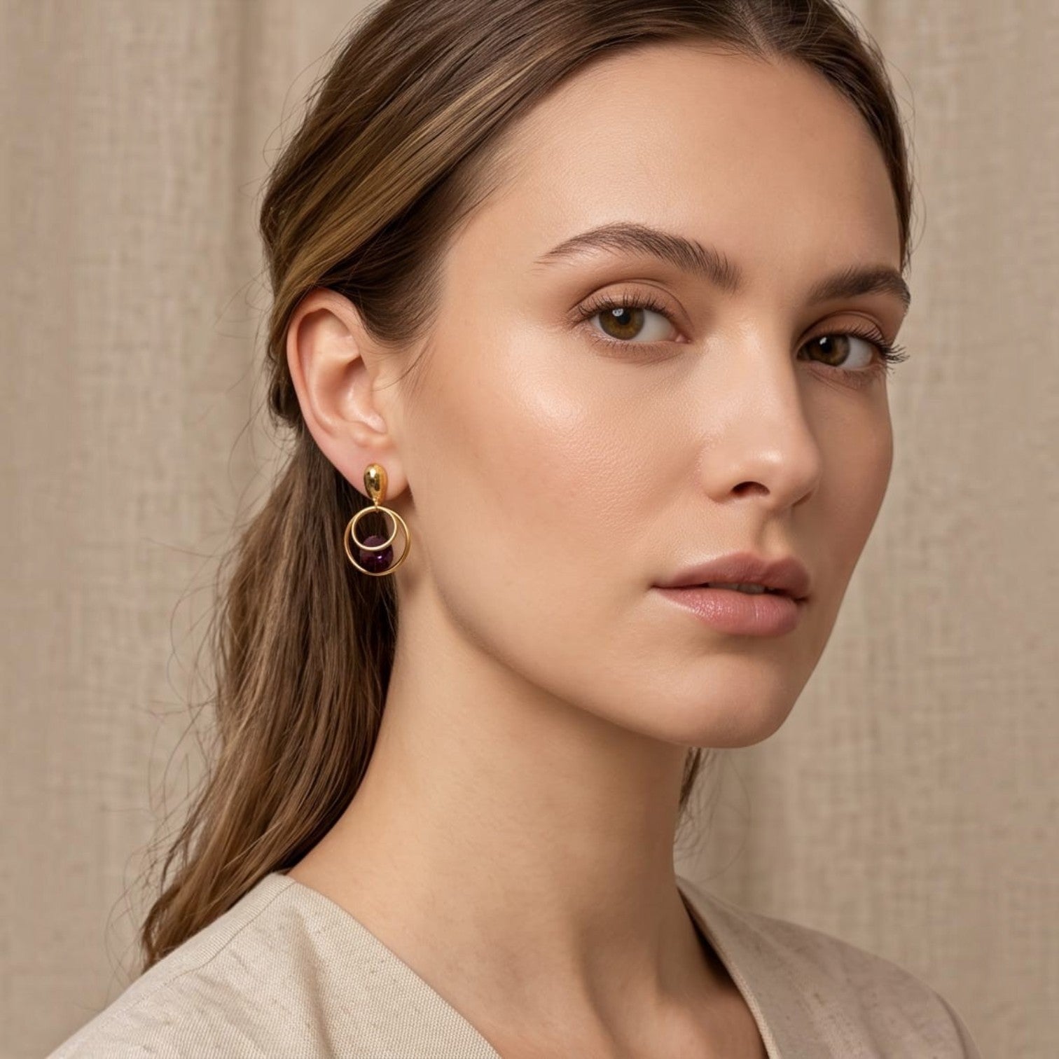 Anzora Jewel Orbit statement earrings featuring nested gold hoops and a deep purple crystal worn by a model.